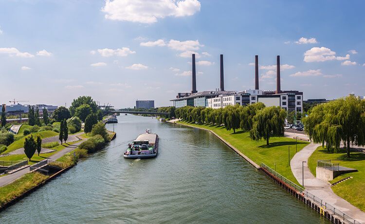 Frachtschiff fährt auf Wasserstraße an einer Fabrik in Wolfsburg vorbei.