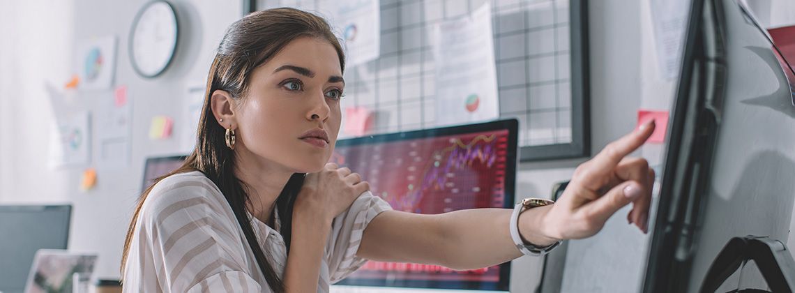 Junge Data Analystin sitzt am Schreibtisch und analysiert Daten am PC.