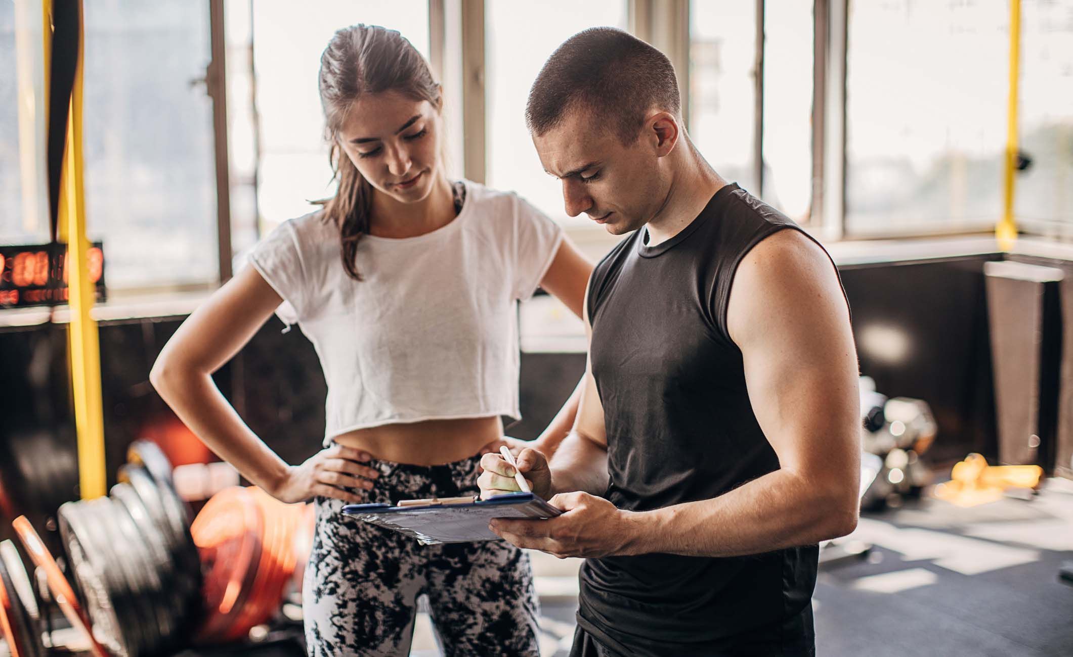 Fitnesstrainer erstellt Trainingsplan für Kundin.