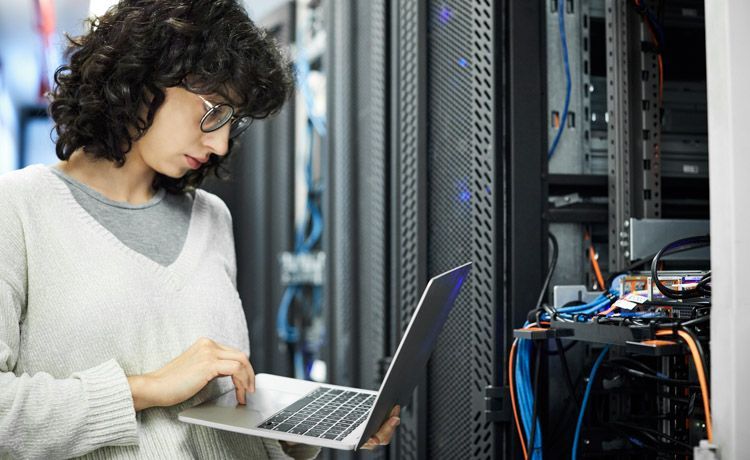 Junge Frau steht mit Laptop vor elektrischen Leitungen.