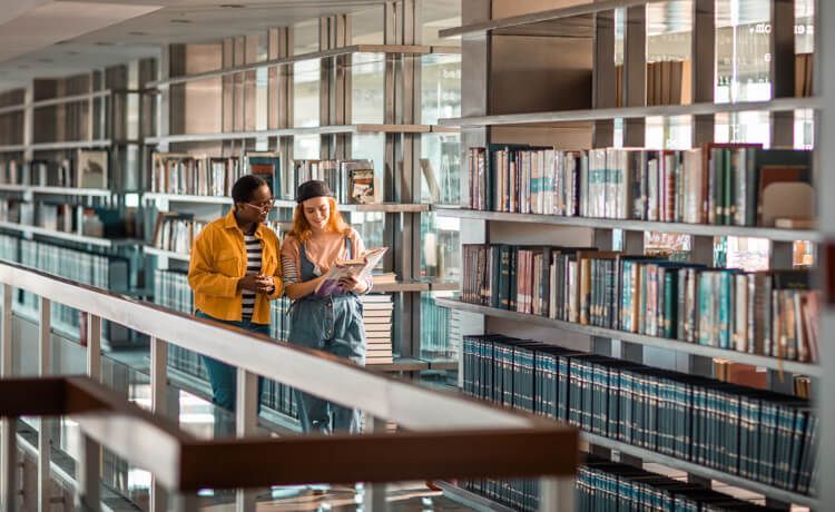 Zwei Studierende des dualen Studiums Hotelmanagement laufen durch die Bibliothek.