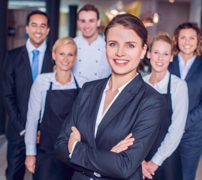 Frau im Anzug und eine Gruppe Menschen gucken in die Kamera.