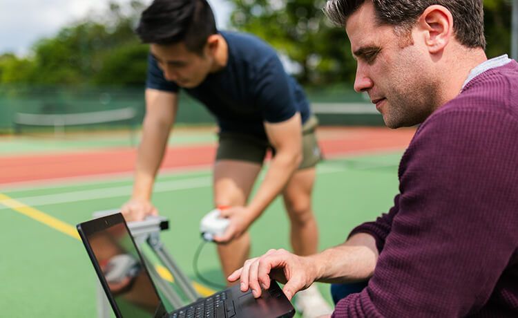 Ein junger Sportinformatiker beim Training mit einem Sportler auf dem Sportplatz