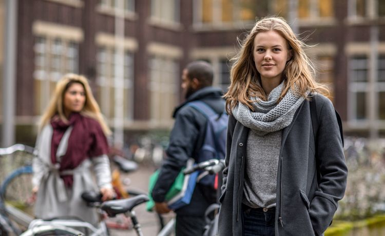 Junge Frau steht vor ihrer Uni.