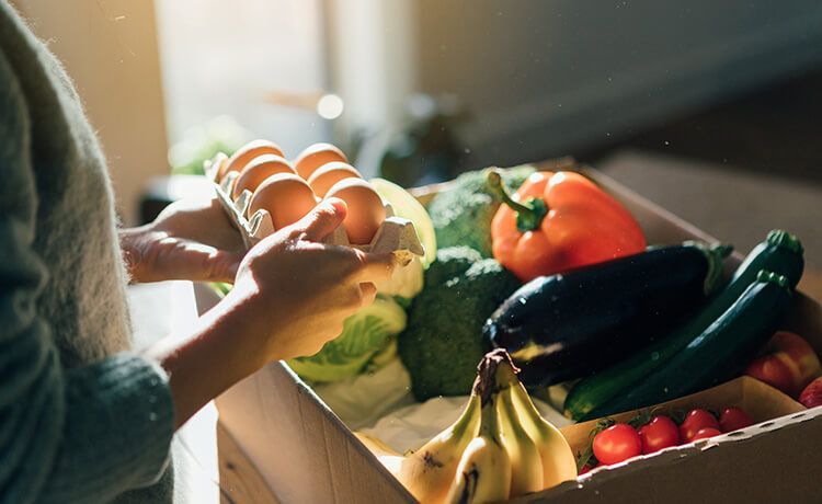 Paket voller gesunder Lebensmittel wie Bananen, Tomaten, Eier, Paprika und Brokoli.