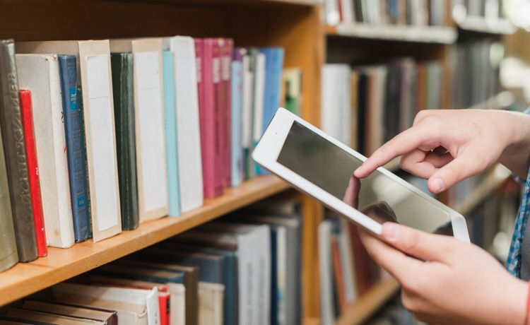 Fachangestellte für Medien- und Informationsdienste kontrolliert mit Tablet den Bücherbestand.