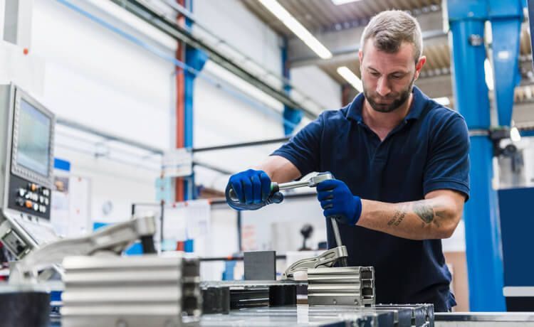 Eine junger Mann arbeitet in einer Arbeitshalle an Metall.