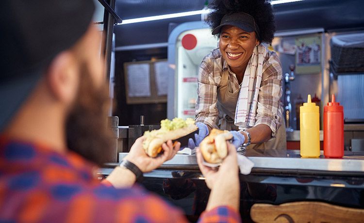 Frau reicht einem Mann Essen aus einem Food-Truck.