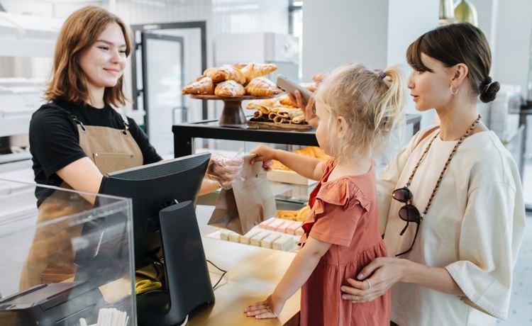 Eine Auszubildende zur Fachverkäuferin Lebensmittelhandwerk bedient eine Mutter mit ihrer Tochter.
