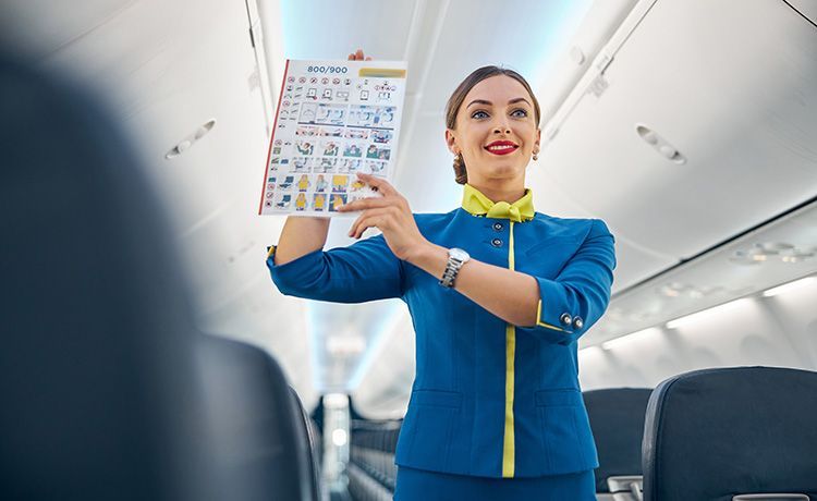 Eine Flugbegleiterin erklärt die Sicherheitsvorschriften im Flugzeug anhand einer Broschüre.