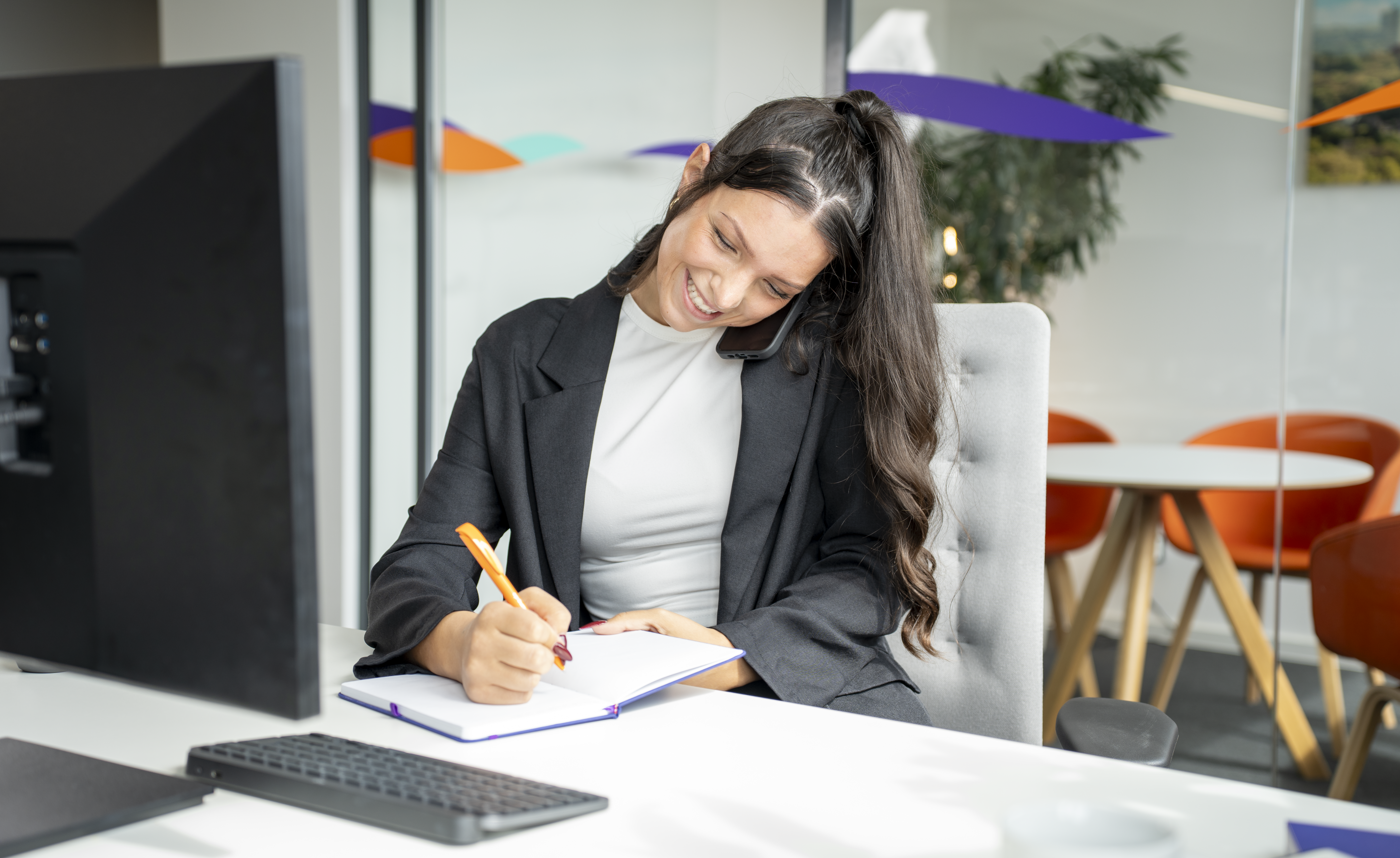 Junge Frau telefoniert im Büro und macht Notizen.