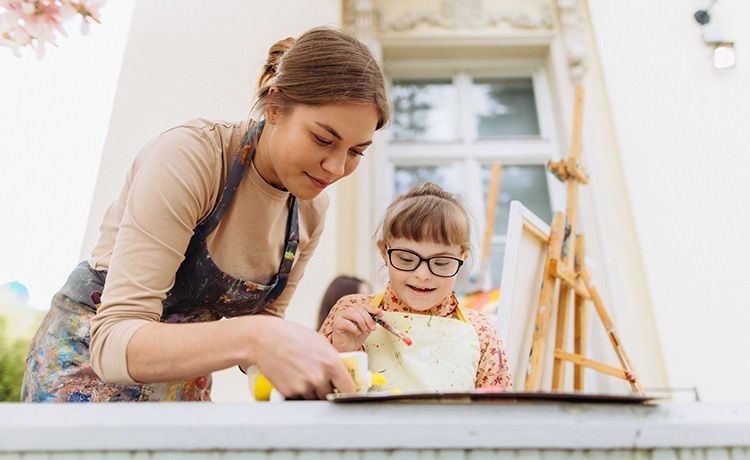 Junge Frau hilft einem Kind beim Malen auf einer Staffelei. Junge Frau hilft einem Kind beim Malen auf einer Staffelei.