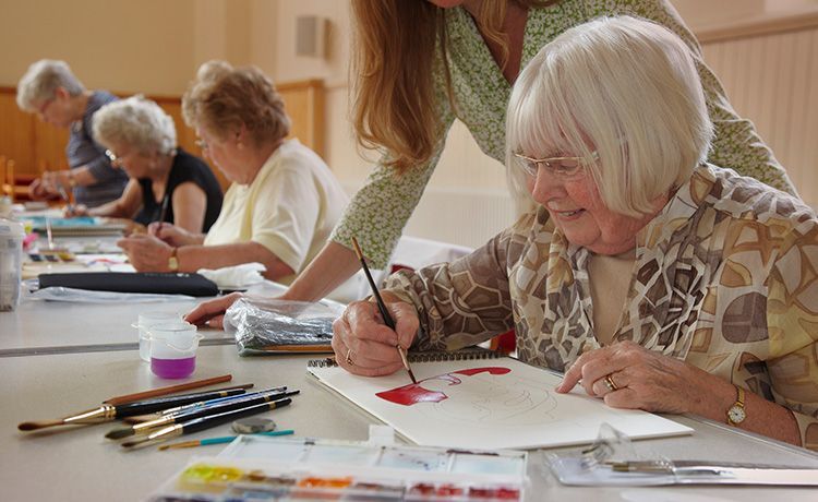 Frau hilft einigen Seniorinnen beim Malen. Frau hilft einigen Seniorinnen beim Malen.