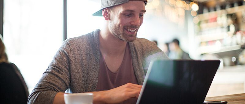 Junger Mann sitzt an einem Tisch und schreibt einen Lebenslauf am Laptop.