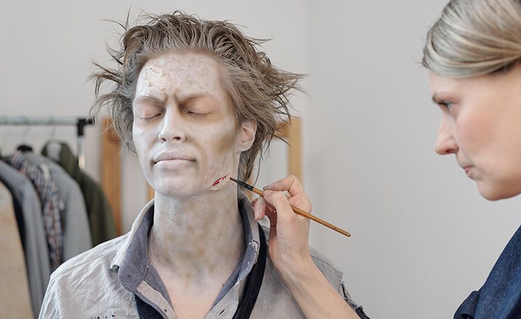 Junge Frau schminkt einem Schauspieler ein Horror-Make-Up.