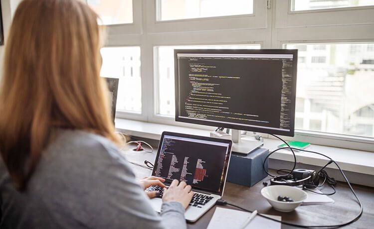 Junge Mathematisch-Technische Softwareentwicklerin sitzt an einem Schreibtisch und arbeitet am Laptop.