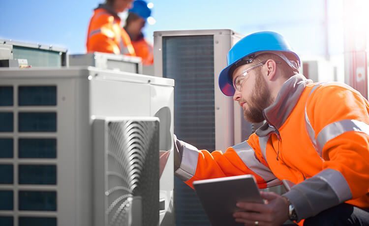 Mechatroniker für Kältetechnik prüft eine Klimaanlage auf einem Dach.