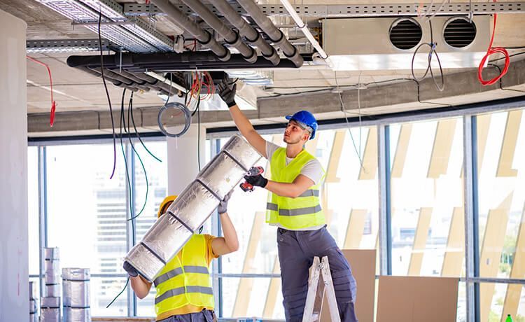 Zwei Mechatroniker für Kältetechnik montieren eine Lüftungsanlage.