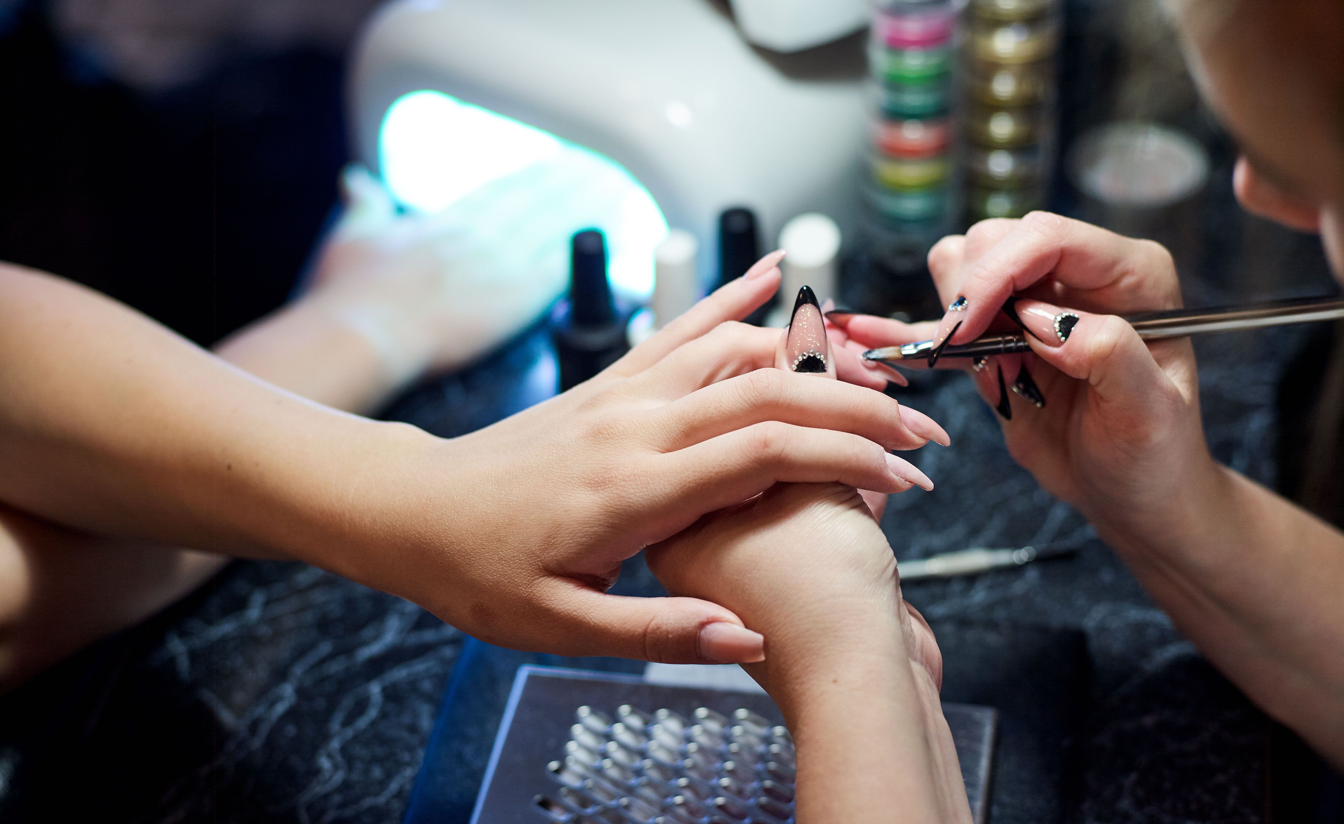 Nahaufnahme einer Frau im Nagelstudio, die von einer Kosmetikerin mit einer Nagelfeile eine Maniküre erhält. Nahaufnahme einer Frau im Nagelstudio, die von einer Kosmetikerin mit einer Nagelfeile eine Maniküre erhält.