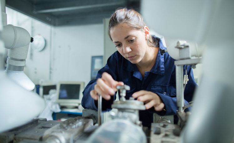 Junge Frau im Blaumann hantiert mit Maschine. Junge Frau im Blaumann hantiert mit Maschine.