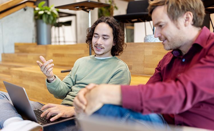 Zwei Social Media Manager sitzen auf einer Treppe und unterhalten sich über eine Kampagne.