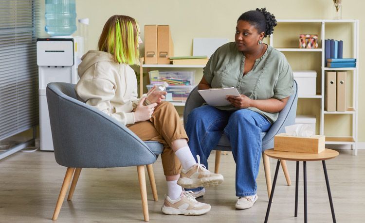 Sozialarbeiterin sitzt im Büro und spricht mit jungem Mädchen über ihre Probleme.
