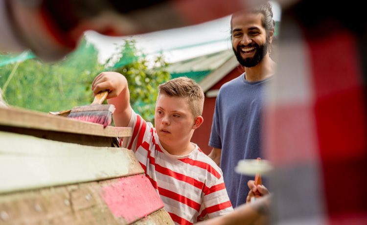 Sozialarbeiter streicht mit Kind Holz.
