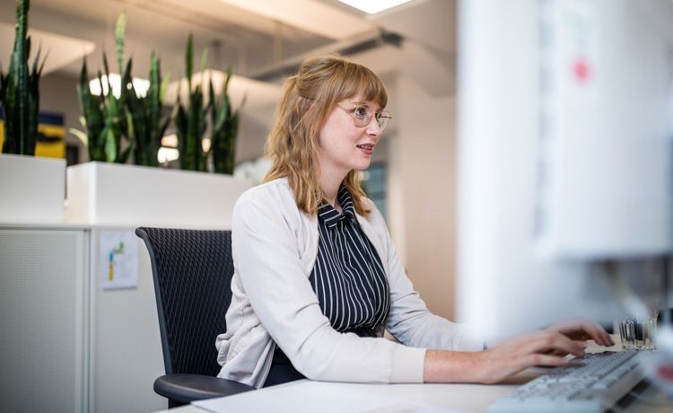 Junge Sozialarbeiterin sitzt am Schreibtisch und erledigt Büroarbeiten am Laptop.