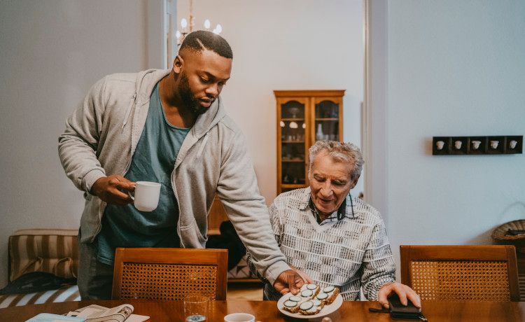Sozialassistent serviert älterem Patienten sein Essen.