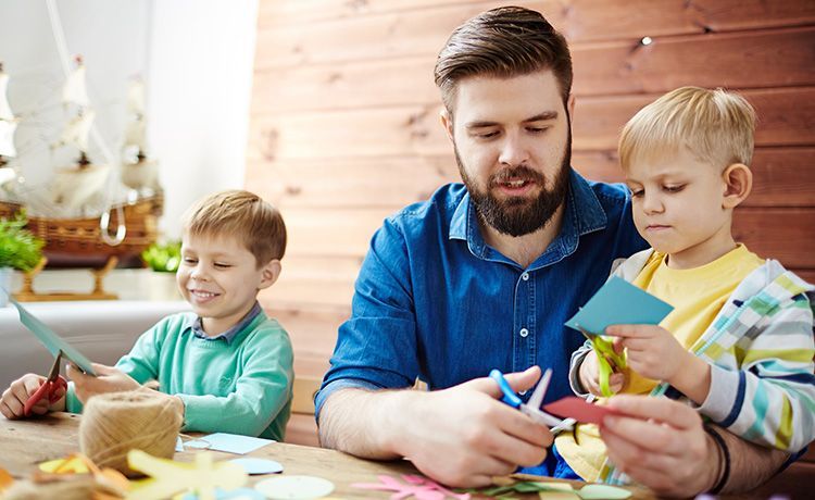 Sozialpädagogischer Assistent sitzt mit zwei Kindern am Tisch und bastelt.