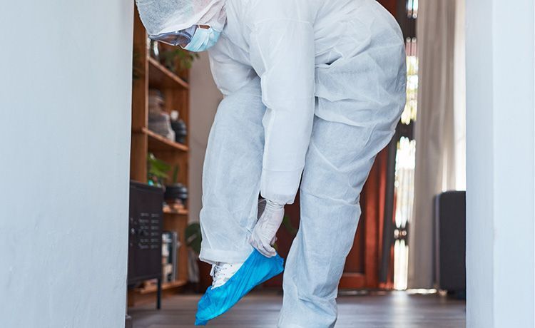 Person im Schutzanzug zieht einen Schutz über die Schuhe.
