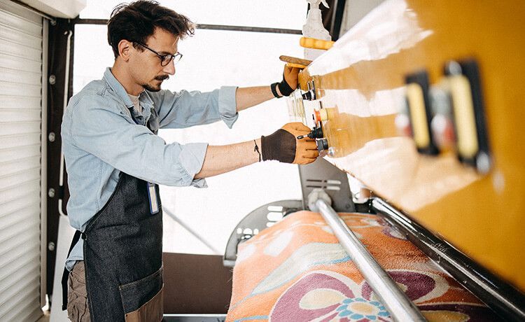 Junger Textilreiniger steht an einer Maschine zum Säubern von Textilien.