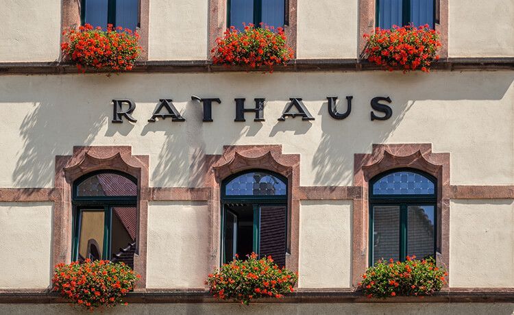 Foto von Rathaus mit schönem Blumenschmuck am Fenster.