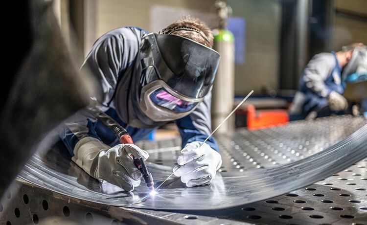 Schweißer steht in der Werkstatt und schweißt ein Metallteil.