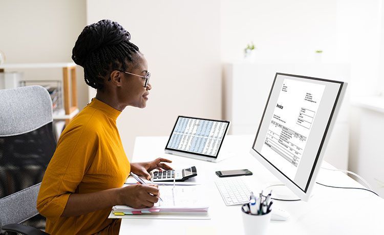 Junge Frau sitzt am PC und überprüft Abrechnungen Junge Frau sitzt am PC und überprüft Abrechnungen