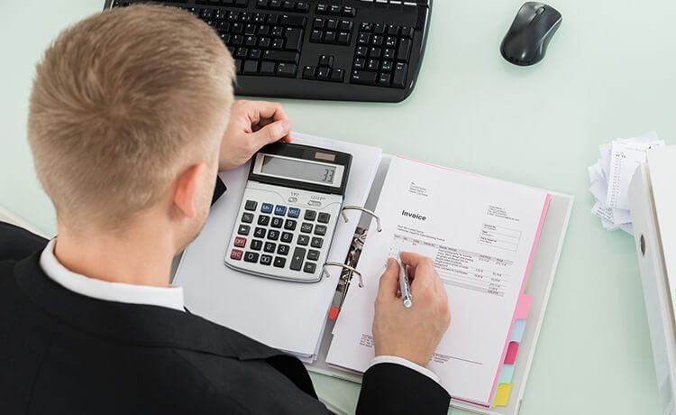 Junger Wirtschaftsprüfer sitzt am Schreibtisch und bearbeitet Rechnungen. Junger Wirtschaftsprüfer sitzt am Schreibtisch und bearbeitet Rechnungen.