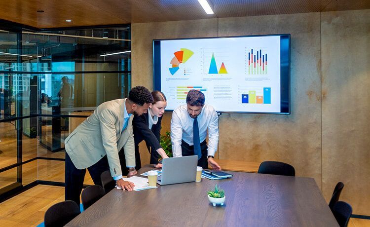 Drei Witschaftsprüfer sind in einem Konferenzraum und schauen auf einen Laptop. Im Hintergrund ist ein Bildschirm mit verschiedenen Tabellen und Schaubildern. Drei Witschaftsprüfer sind in einem Konferenzraum und schauen auf einen Laptop. Im Hintergrund ist ein Bildschirm mit verschiedenen Tabellen und Schaubildern.