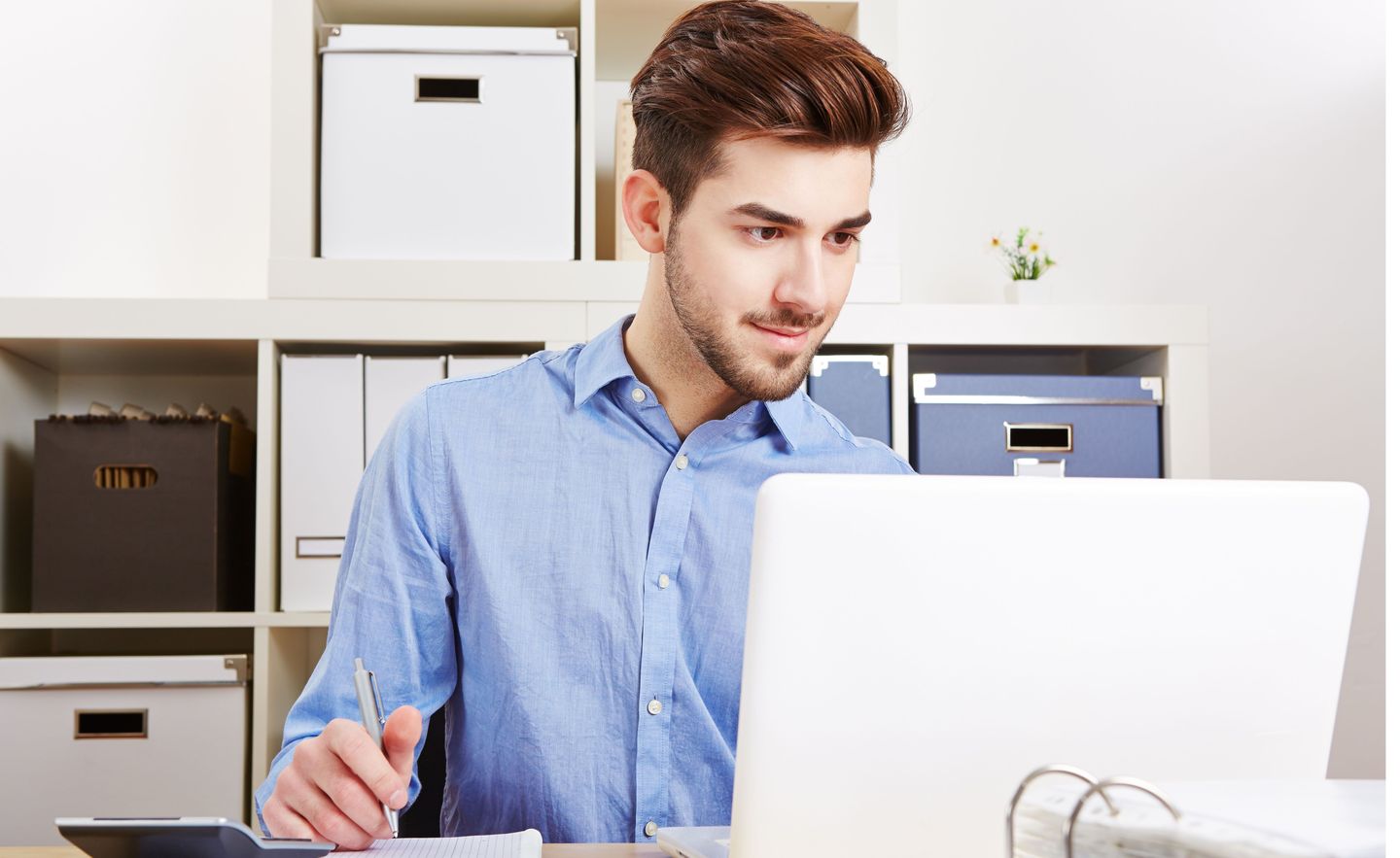 Junger Mann sitzt im Büro am Laptop.