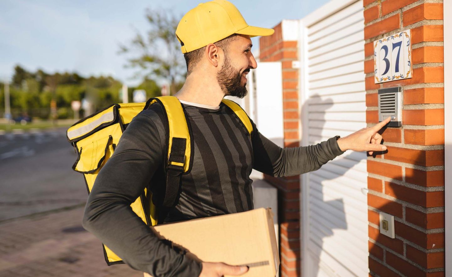Postbote/Paketbote schellt an einer Haustür an und hat ein Paket in der Hand