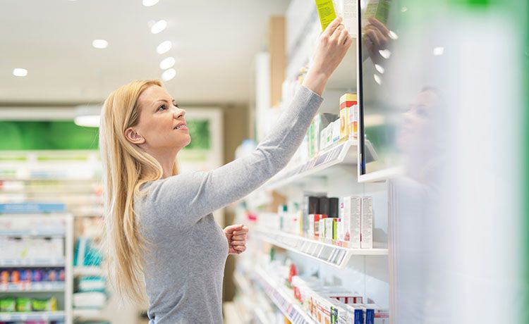 Junge Frau holt eine Packung aus einem Regal in einer Drogerie.