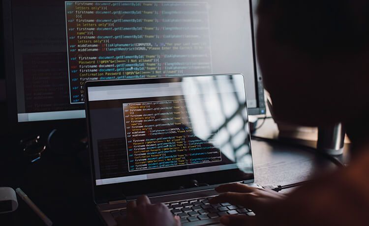 Informatiker sitzt an einem Laptop mit Quellcode und programmiert.