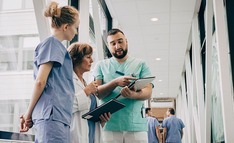 Krankenschwestern und Krankenpfleger stehen im Krankenhaus-Flur und besprechen einen Behandlungsplan für Patienten.
