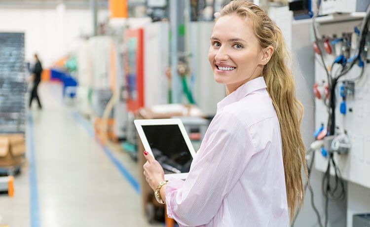 Junge Wirtschaftsprüferin hält ein Tablet in der Hand und lächelt in die Kamera.