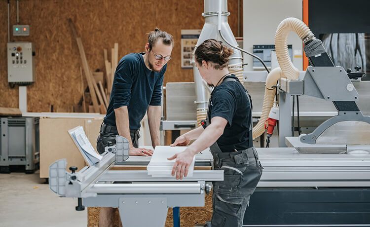 Zwei Zimmerer stehen in der Werkstatt und sägen ein Bauteil zurecht.
