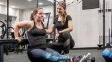 Fitnesstrainerin hilft einer Frau bei einer Übung.