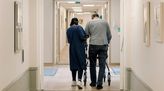 Altenpflegerin läuft mit Patient durch den Flur.