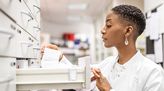 Junge Apothekerin sucht in einem Apothekerschrank nach einem Medikament.