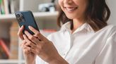 Social Media Managerin blickt lächelnd auf ein Smartphone, das sie in den Händen hält.