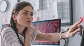 Junge Data Analystin sitzt am Schreibtisch und analysiert Daten am PC.