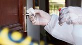 Jemand reinigt an einem Tatort eine Türklinke und trägt dabei Schutzkleidung.